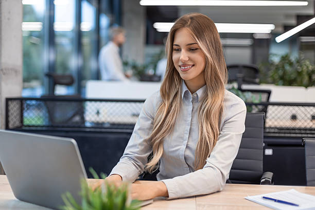 istock Young business woman is using laptop while sitting in the office, smiling 2243384276