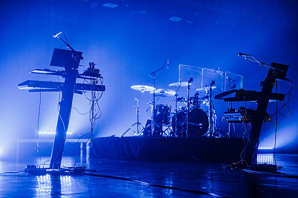 istock Dimly lit concert stage setup featuring a drum kit, keyboards, microphones, and music equipment under blue lighting. Clear copy space above the instruments 2243385221