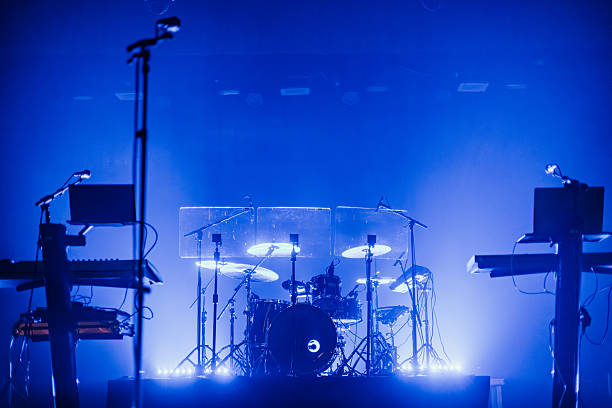 istock Dimly lit concert stage setup featuring a drum kit, keyboards, microphones, and music equipment under blue lighting. Clear copy space above the instruments 2243385231