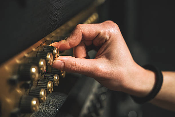 Male hand with long nails turning knob on a guitar amplifier, live music studio recording rock metal session, guitar player musician