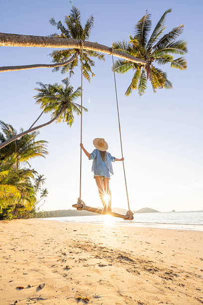 istock Woman Swinging on Palm Tree Beach at Sunrise 2243387812