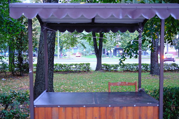 A wooden market stall is empty in a park on a cloudy day.