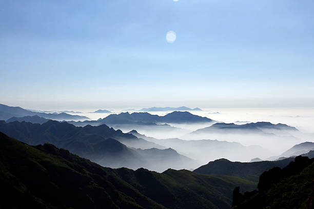 A scenic view of misty mountain peaks under a clear sky with the sun shining, showcasing a beautiful natural landscape.