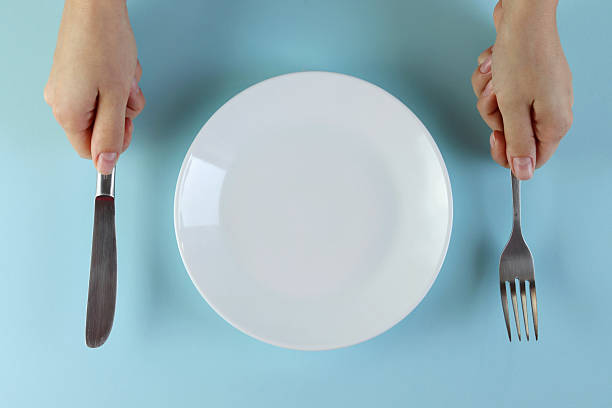 istock Hands holding a knife and fork next to an empty white plate on a blue background. 2243389782