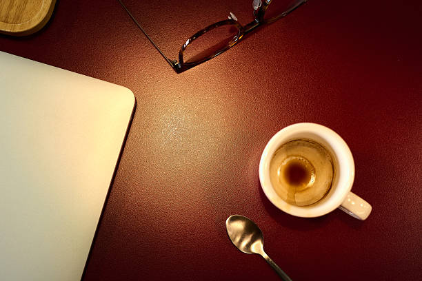 Soft light on a red textured desk shows a laptop corner, eyeglasses, teaspoon and an espresso cupminimal scene for productivity, remote work and creative workflow ideas.