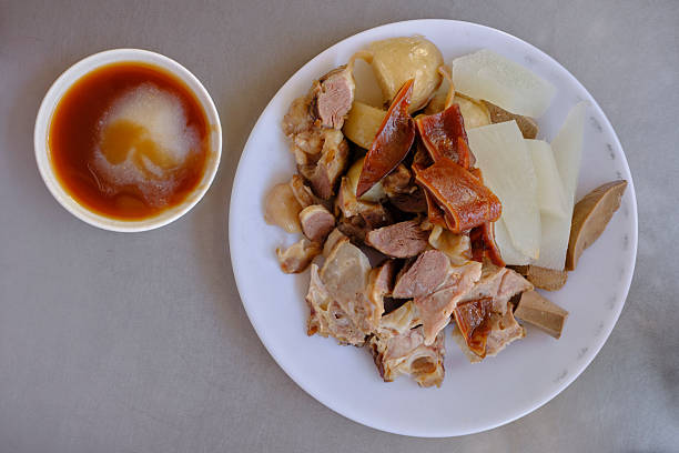Overhead view of a classic Tainan black-and-white cut (xiangchang shourou) platter: assorted boiled/poached pork cuts and offal with daikon on a white plate, served with a sweet soygarlic dipping sauce. Clean, brand-free composition on a stainless tabletop.