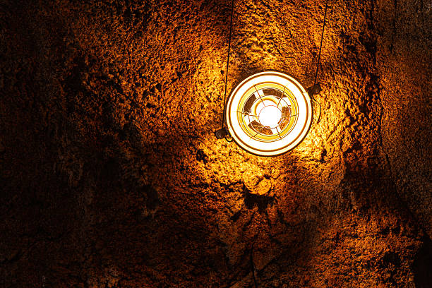 A ceiling lighting lamp in metal retro design was installed at the rock mine industrial workplace, it glowing in orange warm light shade.