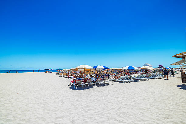 Miami Beach. USA. April.15.2025. Tourists relaxing on lounge chairs under umbrellas on Miami Beach facing the Atlantic Ocean in bright sunlight.