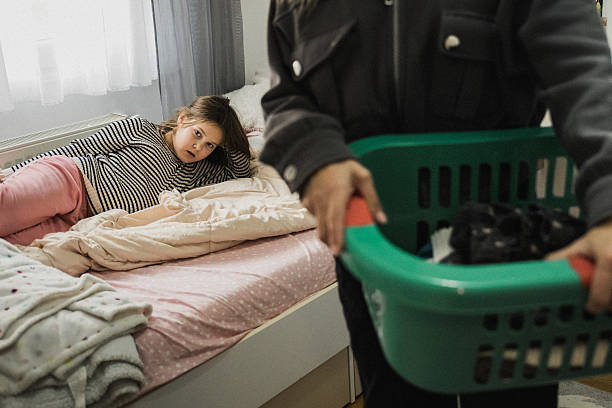 istock Mother, picking up clothes from her daughter's room into laundry basket while her daughter is resting. 2243402574