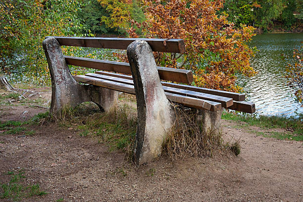 An old, rustic wooden and stone bench by the edge of Dreiburgensee lake. A peaceful spot for rest and contemplation in nature.