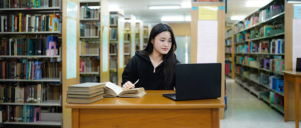 istock Young college woman working on his computer while studying in the library alone. 2243405714