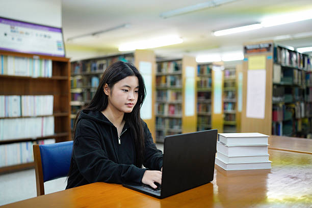 istock Young college woman working on his computer while studying in the library alone. 2243405722