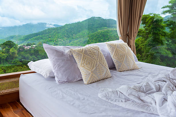 istock Cozy white unmade bed with decorative pillows in a glass room with panoramic mountain view, luxury nature resort concept. Perfect for themes of travel, relaxation, eco-friendly resorts, and peaceful retreats. 2243410204