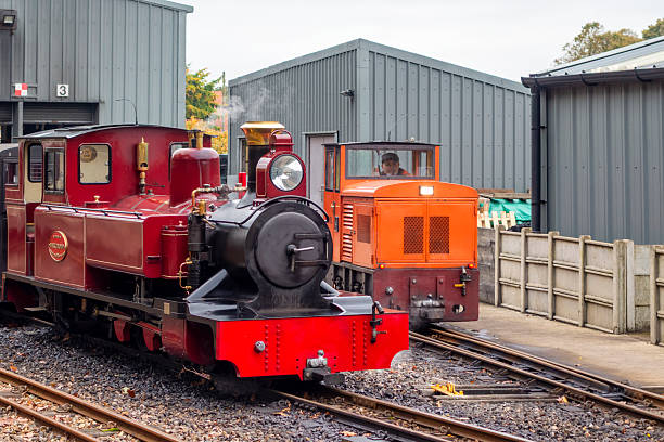 Aylsham, Norfolk, United Kingdom: October 15, 2024: ‘Rusty’, a narrow gauge railway diesel engine which is used for shunting, moving along the track behind ‘Mark Timothy’, a steam engine used for pulling passenger trains. The 15” Bure Valley Railway runs between Aylsham and Wroxham in Norfolk, Eastern England; it uses steam, electric and diesel engines and stops at Brampton, Buxton and Coltishall on its way to Wroxham in the heart of the Norfolk Broads. The Bure Valley Railway opened in 1990 and has been a popular tourist attraction ever since.