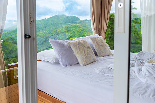 istock Cozy white bed with decorative pillows in a glass room with panoramic mountain view, luxury nature resort concept. Perfect for themes of travel, relaxation, eco-friendly resorts, and peaceful retreats. 2243412650