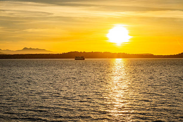 A ferry ship is captured transporting people across the water, silhouetted against a stunning golden sunset