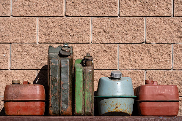 Many old rusty iron fuel cans on a table near the garage, close up. Various metal painted canisters for gasoline, retro style