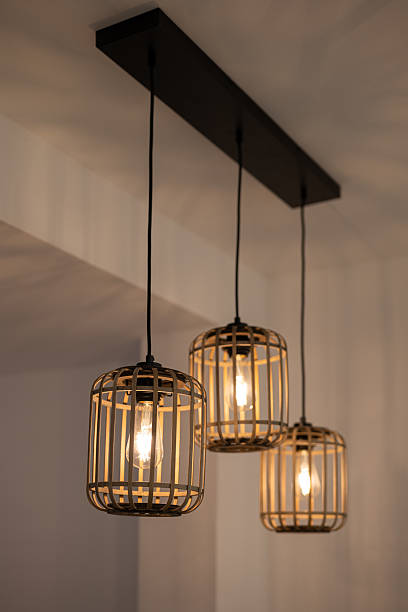 istock Three pendant lights with a cage design hang from a black ceiling fixture. The lights emit a warm glow, enhancing the modern interior decor. 2243416030