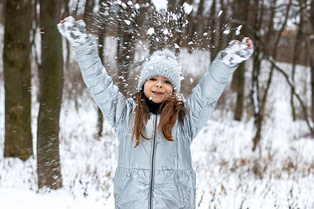 istock Girl in a silver winter coat throws snow joyfully in a forest setting, capturing carefree outdoor fun 2243416501