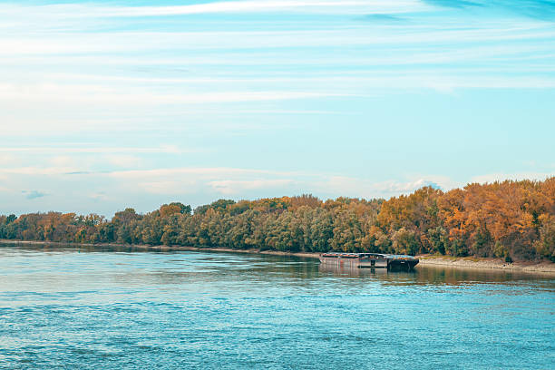 Cargo barge floating on the Danube River at sunset during calm autumn evening. Selective focus.
