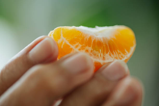 Close-up of senior hand holding a peeled orange fruit.