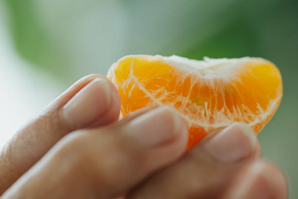 Close-up of senior hand holding a peeled orange fruit.