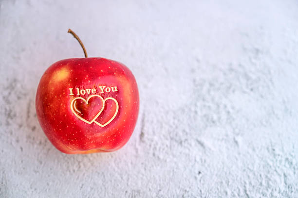 Stock photo showing close-up view of red Honeycrisp apples, one with a heart-shaped hole cut into it's flesh. Romantic snack and wellbeing concept