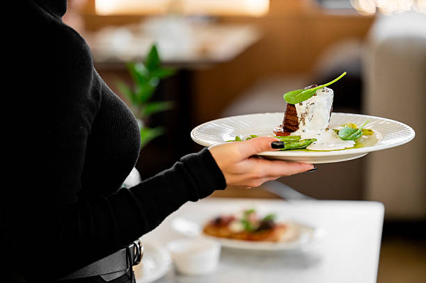 istock A server in a black uniform presents a gourmet dish on a white plate in a restaurant setting. The dish is garnished with a creamy sauce and green leaves 2243424474