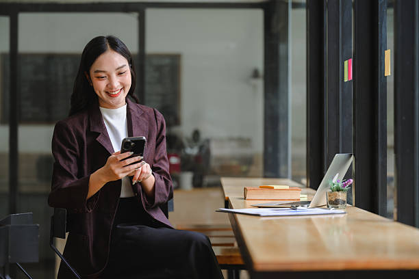 istock Young Asian woman smiling, using smartphone while working remotely at a coffee shop or coworking space 2243424961