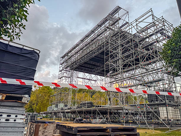 istock Construction site with scaffolding and safety barriers. Metal framework for a stage under assembly. Trees and cloudy sky in the background. 2243429871