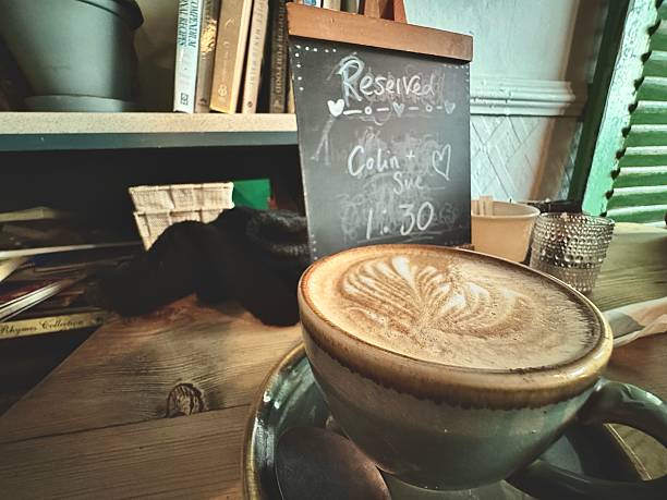 A blackboard style message stating that the restaurant table is reserved, with green wooden shutters in the background and a cup of coffee with froth art on a wooden table