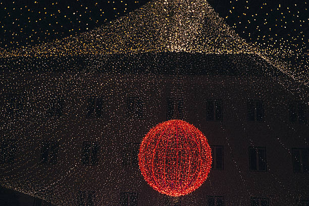 Bright red spherical light decoration is surrounded by shimmering fairy lights, illuminating the urban scene at night, enhancing the festive ambiance and visual charm