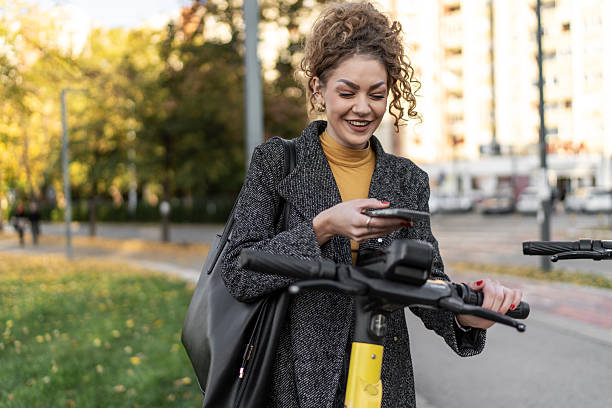 istock Woman smiling using smartphone to rent electric scooter 2243445066