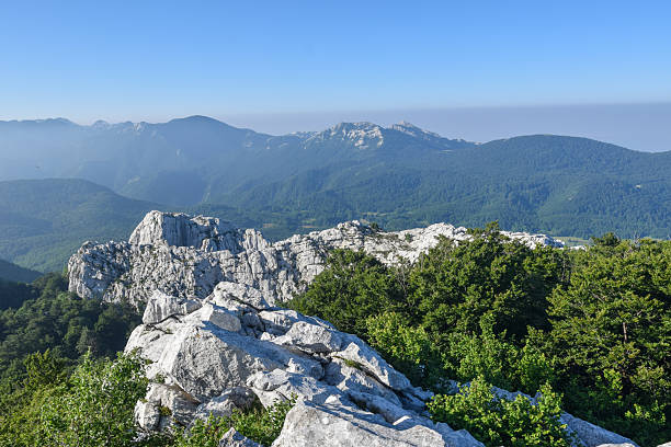 istock Mountain view with rocky cliffs, green forests, and distant hazy peaks under a clear sky 2243445270