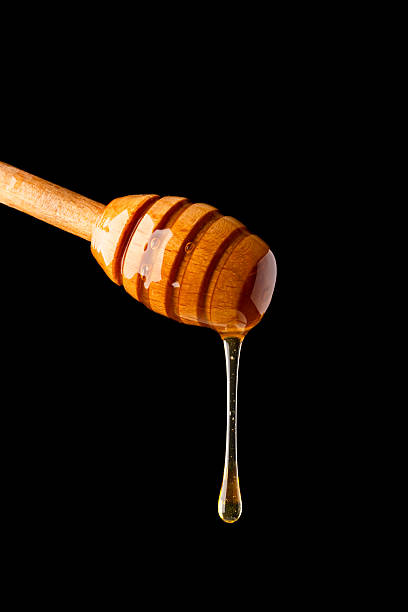 istock Honey dripping from honey dipper on black background 2243445733