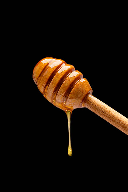 istock Honey dripping from honey dipper on black background 2243446010