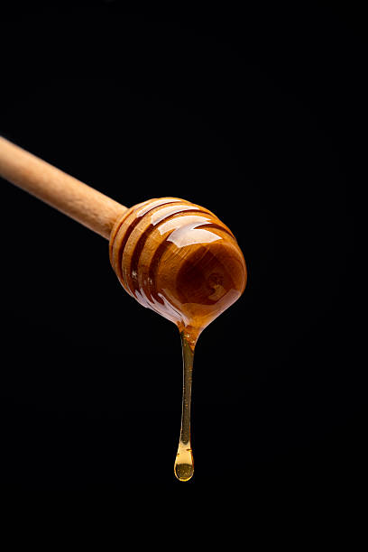 istock Honey dripping from honey dipper on black background 2243446028