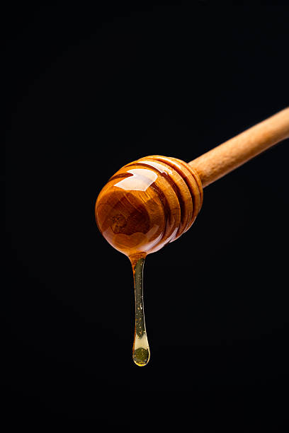 istock Honey dripping from honey dipper on black background 2243446036