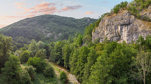 istock Aerial view discovering a lush green river valley, dense forests, and rocky mountains under a warm sky. Nature landscape 2243447981