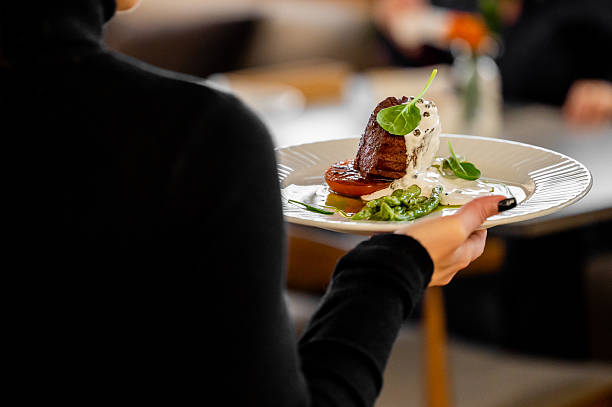 istock An elegantly plated gourmet dish, possibly a beef fillet with roasted vegetables and a creamy sauce, is being held by a server in a fine-dining restaurant 2243449930
