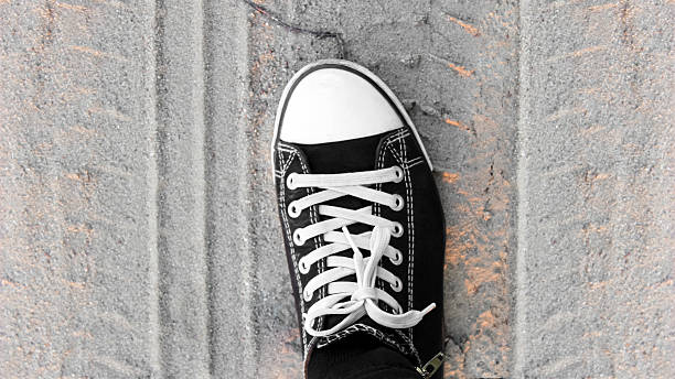 Photo of a black sneaker-type shoe with a leg against the background of a sandy field road with tractor tracks.