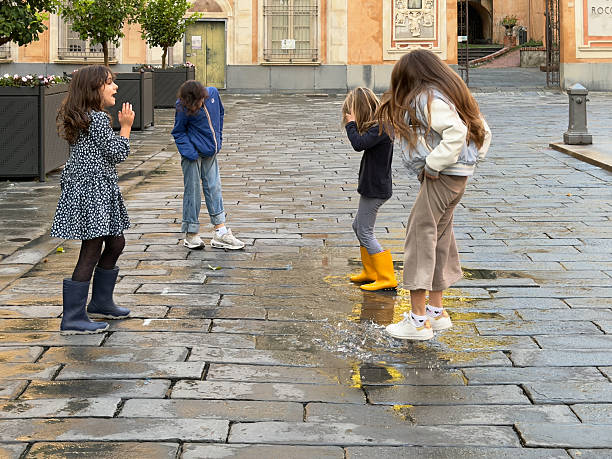 Chiavari, Italy -  October 20,  2025 -A group of children happily playing, jumping into a puddle on the pavement of Piazza Matteotti.