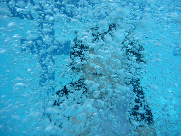 Person obscuring face with hair and bubbles while submerging in blue swimming pool water