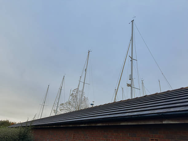 Tall yacht masts rising above a marina building roof against pale blue sky.