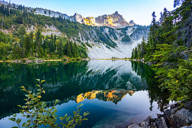 A scenic view captures mountain peaks beautifully reflecting in the emerald waters of Snow Lake at sunset in Mount Rainier National Park, Washington.