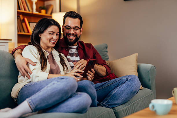 istock Happy couple relaxing on sofa and using smartphone 2243460518