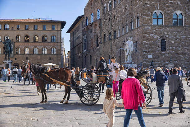 Piazza della Signoria on an autumn afternoon, Florence, Italy. Crowd of tourist walking around including a horse-drawn carriage. Neptune fountain in the background.