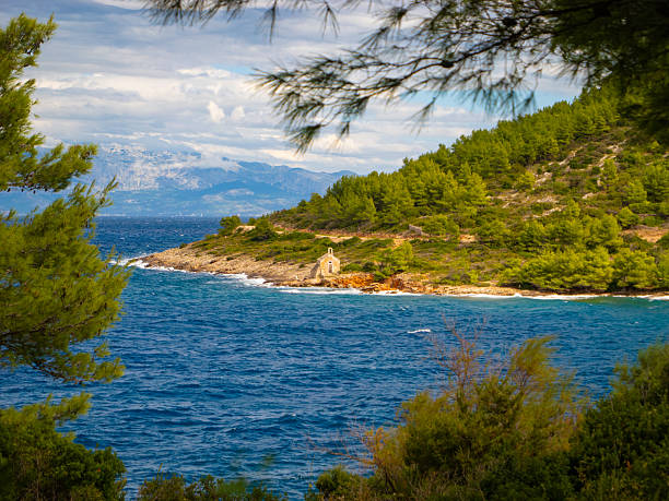 istock Framed by pine branches, stone chapel stands on rugged shore above rough sea 2243466158