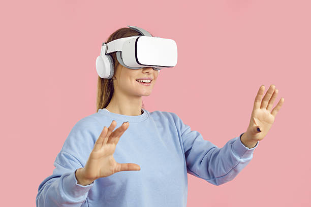 istock Smiling amazed young woman touching air during VR experience, isolated on pink background. 2243469603