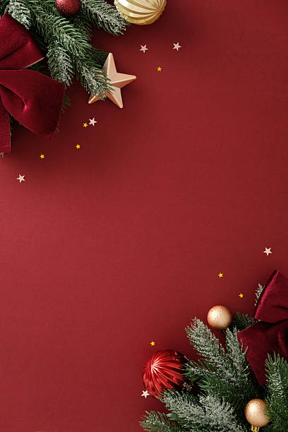 istock Decorated pine branches with red bows, gold ornaments, and star confetti frame a deep red background, perfect for luxurious Christmas cards and festive promotional designs. 2243469960